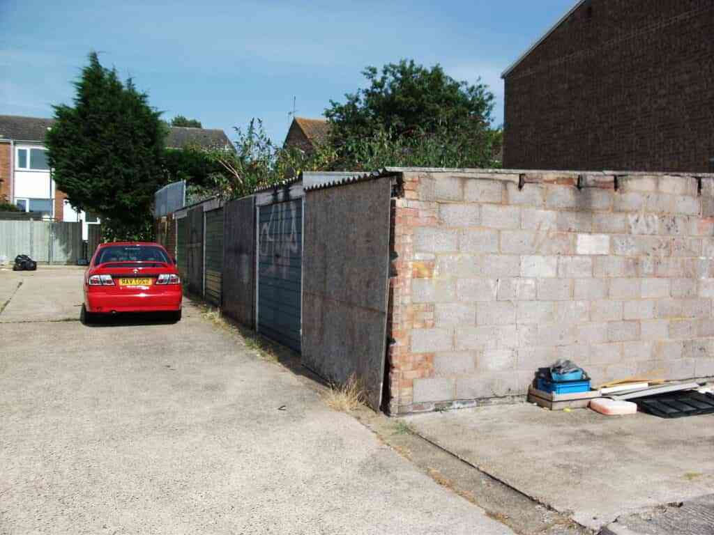 Battery Garage Refurbishment before with red car infront of garages